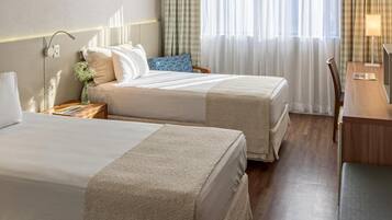 Quarto de hotel com duas camas, uma escrivaninha e uma cadeira.