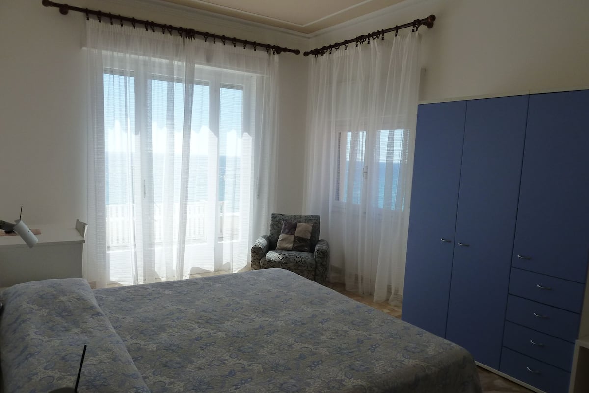 Ein Schlafzimmer mit einem Bett, einem Stuhl, einem Kleiderschrank und durchsichtigen Vorhängen.