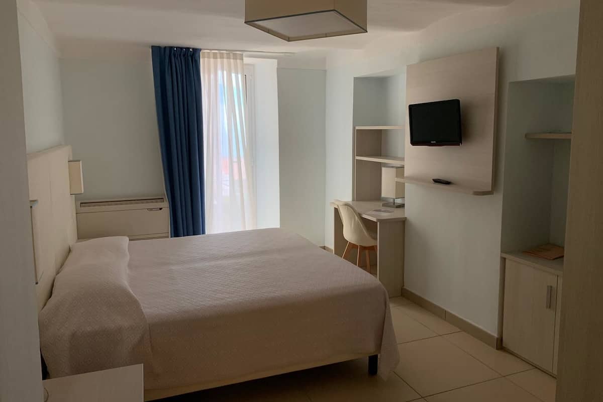 Ein Hotelzimmer mit Bett, Schreibtisch, Stuhl, Fernseher und Kleiderschrank.