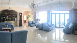 A spacious lobby with blue armchairs, a chandelier, a clock, and a reception desk. - La Balnearia (Alassio)