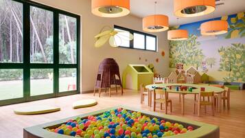A children's playroom with a ball pit, large windows, and orange pendant lights.