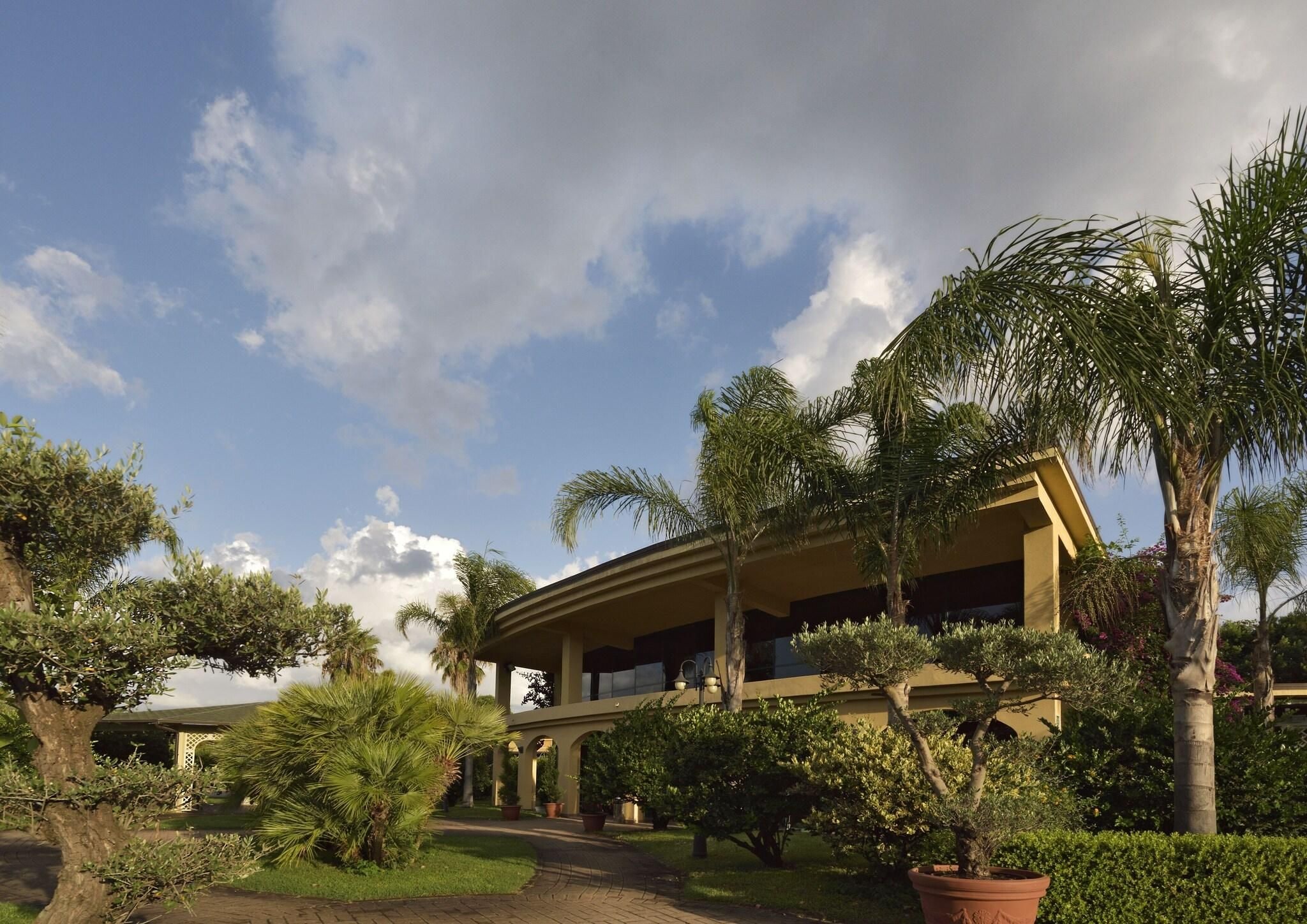 A building with a covered outdoor area, surrounded by palm trees and other greenery.