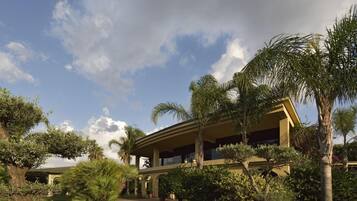 A building with a covered outdoor area, surrounded by palm trees and other greenery.