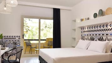 A hotel room with a bed, a desk with a chair, a balcony with chairs, and decorative wall art.