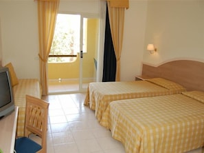 Habitación de hotel con dos camas, televisión, una silla y balcón con cortinas.