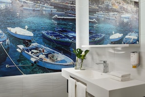 Une salle de bain avec une grande fresque représentant des bateaux sur le mur, un lavabo blanc et un miroir.