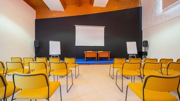 A conference room with yellow chairs, a stage with a white screen, and two whiteboards.