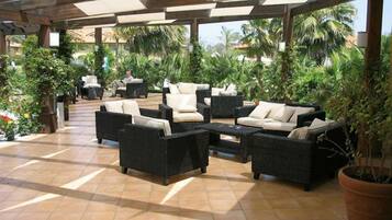 An outdoor patio area with wicker furniture, a tiled floor, and potted plants.