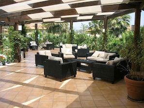 Un patio al aire libre con mobiliario de mimbre, piso de baldosas y plantas en macetas.
