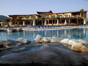 Een resort met een zwembad, ligbedden en een gebouw in traditionele architectuur.