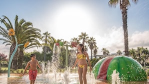 Un espace de jeux aquatiques doté de plusieurs jets d’eau et d’un grand toboggan aquatique vert.