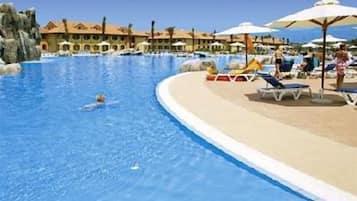 Una piscina con lettini e ombrelloni, circondata da edifici in stile architettonico mediterraneo.