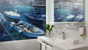 Un baño con un gran mural de barcos, un lavamanos blanco, un perchero y un dispensador de jabón.