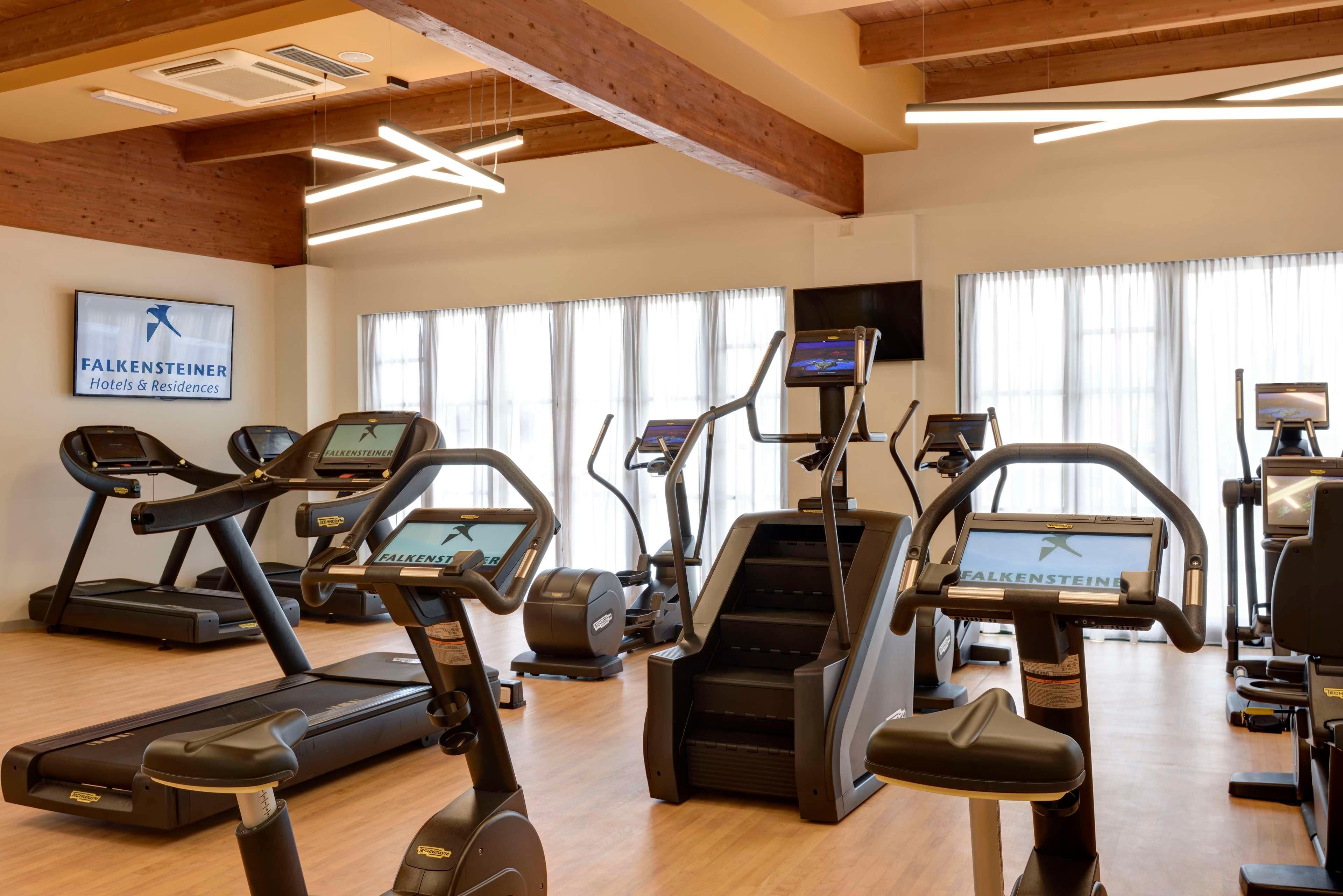 A gym with treadmills, ellipticals, and a TV screen.