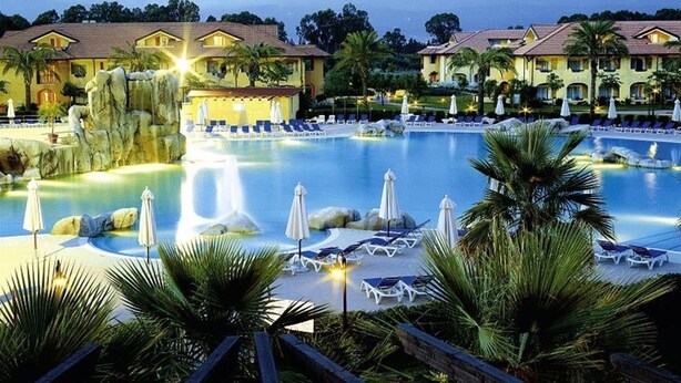 Un resort con una amplia piscina, sillas de descanso, sombrillas y una cascada.