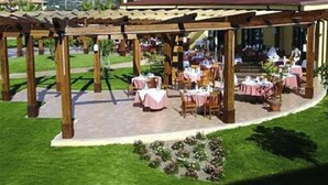 Un restaurante al aire libre con mesas y sillas, una estructura de pérgola y vistas a colinas distantes.