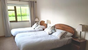 A hotel room with two single beds, a wooden headboard, bedside lamps, a window with curtains, and a carpeted floor. - Valley Lodge (Kilcoman)