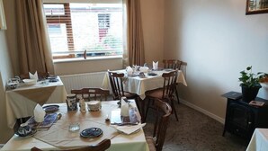 A dining area with multiple tables and chairs, a window with blinds, and a radiator. - Valley Lodge (Kilcoman)