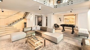 A spacious living area with a modern sofa set, a glass coffee table, and a foosball table. A staircase with glass railings leads to an upper level. - the DOUGLAS, Autograph Collection (Vancouver)