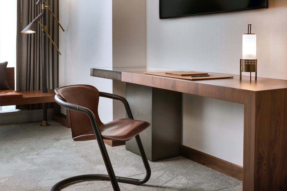A modern office space with a wooden desk, a leather chair, a standing lamp, and a flat-screen TV mounted on the wall.