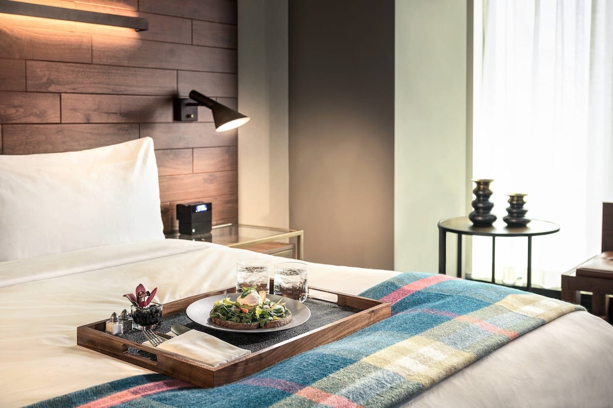 A neatly made bed with a tray of breakfast, a bedside lamp, and a small table with decorative items.