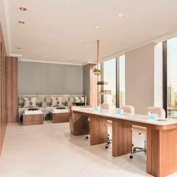 A modern office space with a long wooden conference table, a sofa area, and large windows offering a city view.
