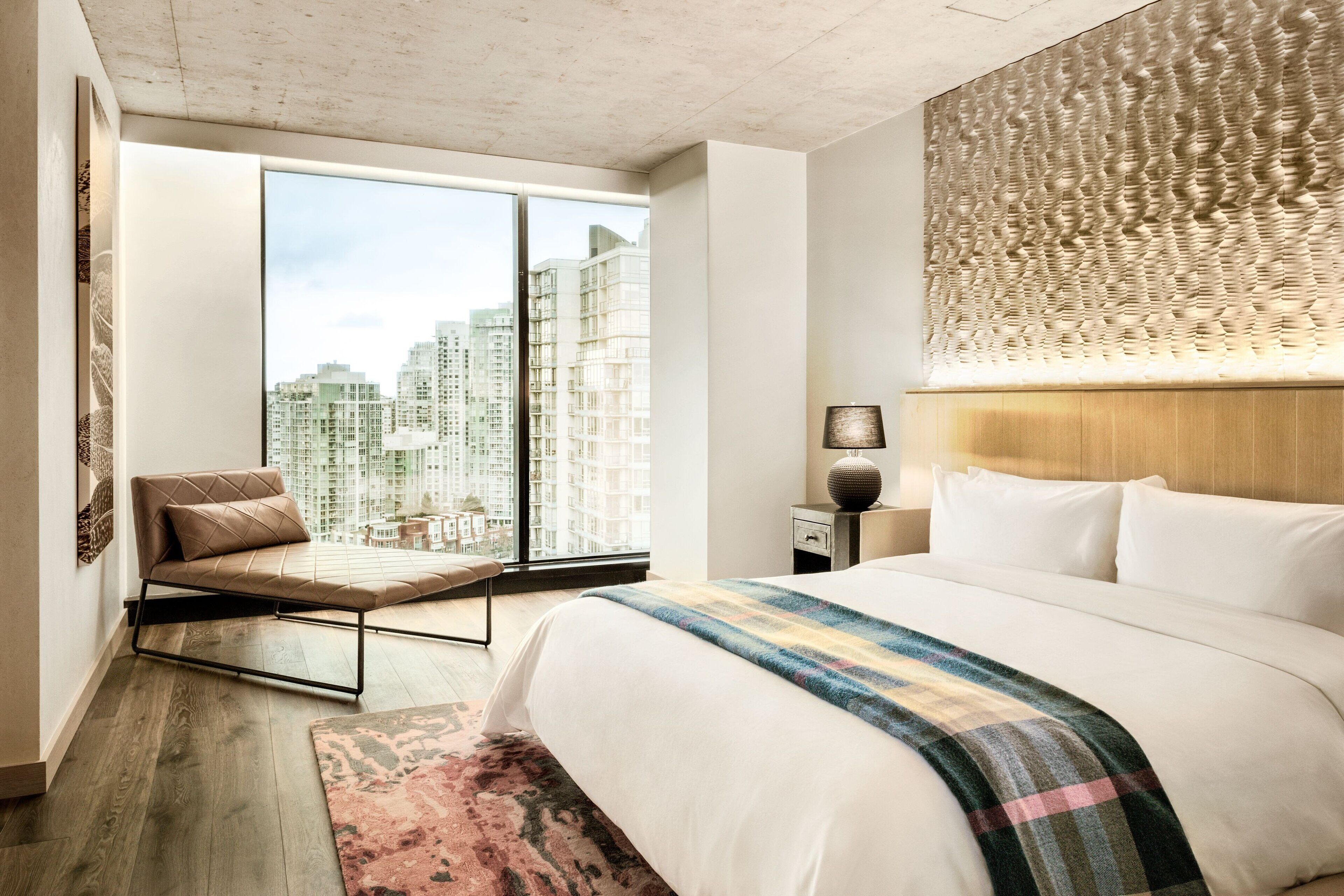 Quarto de hotel moderno com uma cama grande, área de estar e vista para a cidade.