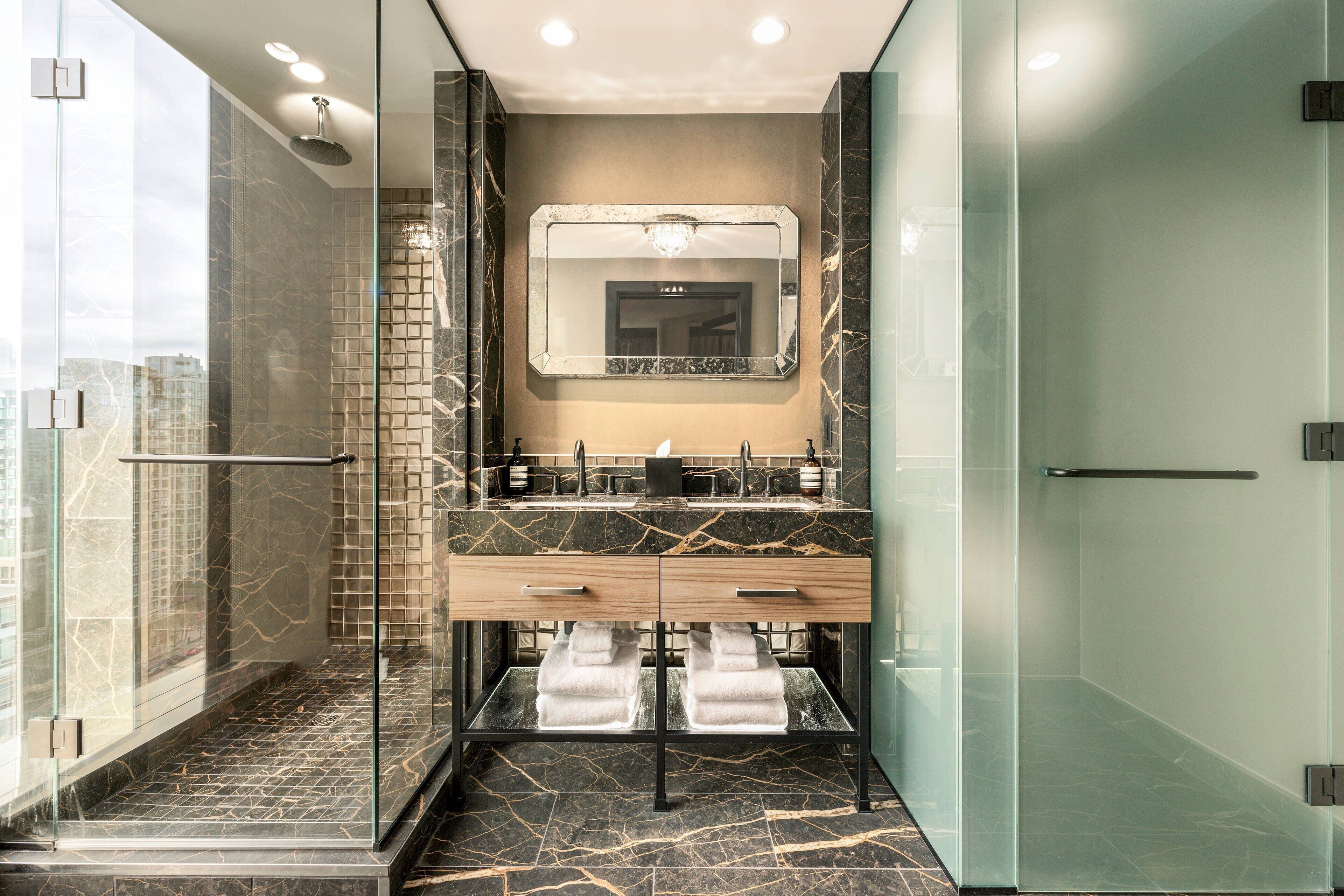 A modern bathroom with a glass shower enclosure, a marble-tiled floor, and a dual sink vanity with a mirror above.