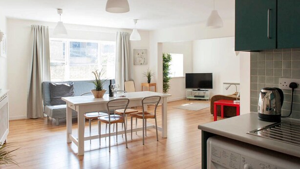Una cocina moderna con lavavajillas, una mesa roja y un televisor al fondo.