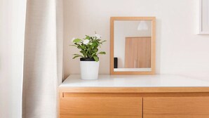Un tocador de baño con encimera blanca, un mueble de madera, una planta en maceta y un espejo.