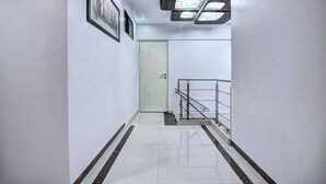Corredor limpo e moderno, com paredes brancas, piso em azulejos e um corrimão metálico no final.