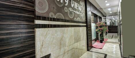 A hotel lobby with a 'CITY VIEW' sign, marble flooring, and a reception area with a red carpet and potted plants.