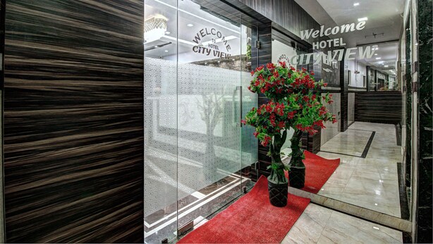 Entrada de hotel moderna com tapete vermelho, placa de boas-vindas e planta em vaso.