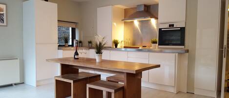 Eine moderne Küche mit einem Holzespeisetisch und Bänken, weißen Schränken und einem Bosch-Backofen.