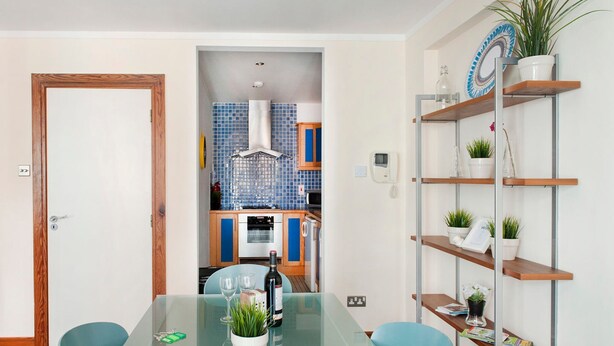 A modern kitchen with blue tiles, a central island, and a dining area with a glass table and blue chairs. - MetroStays - Temple Bar 18 (Dublin)