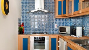 A kitchen with blue tiles, stainless steel appliances, wooden cabinets, and a microwave. - MetroStays - Temple Bar 18 (Dublin)