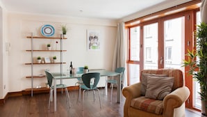 A cozy living room with a wooden floor, a glass dining table, and a sofa with cushions. There are shelves with plants and a framed picture on the wall. - MetroStays - Temple Bar 18 (Dublin)