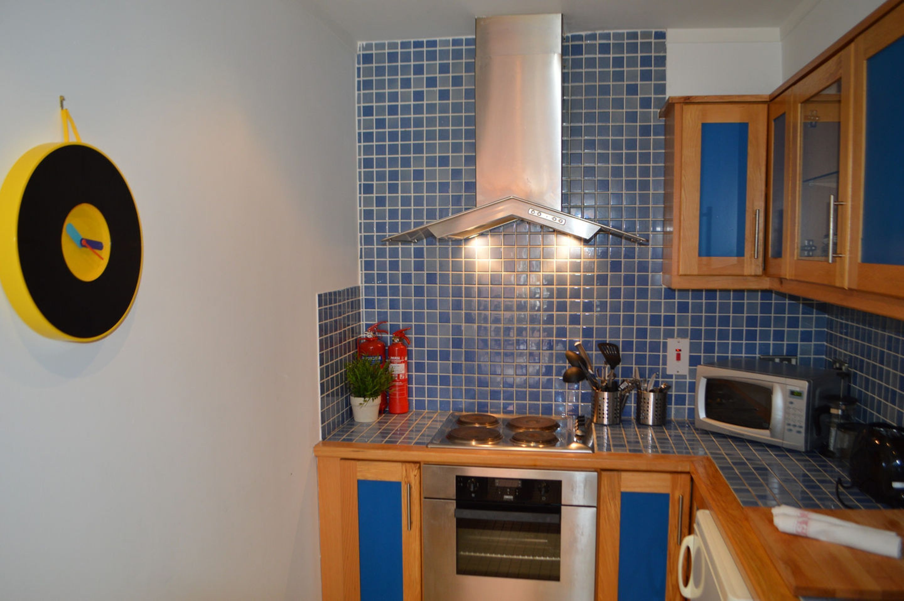 A kitchen with blue tiles, stainless steel appliances, wooden cabinets, and a yellow target on the wall.