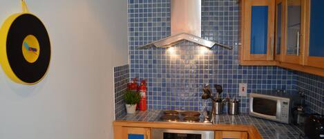 A kitchen with blue tiles, stainless steel appliances, wooden cabinets, and a yellow target on the wall.