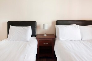 Uma cama de casal com lençóis brancos, um criado-mudo de madeira com uma luminária e uma gaveta.