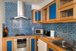 Cozinha com painel de azulejos azuis, armários de madeira e eletrodomésticos de aço inoxidável, além de uma pia.