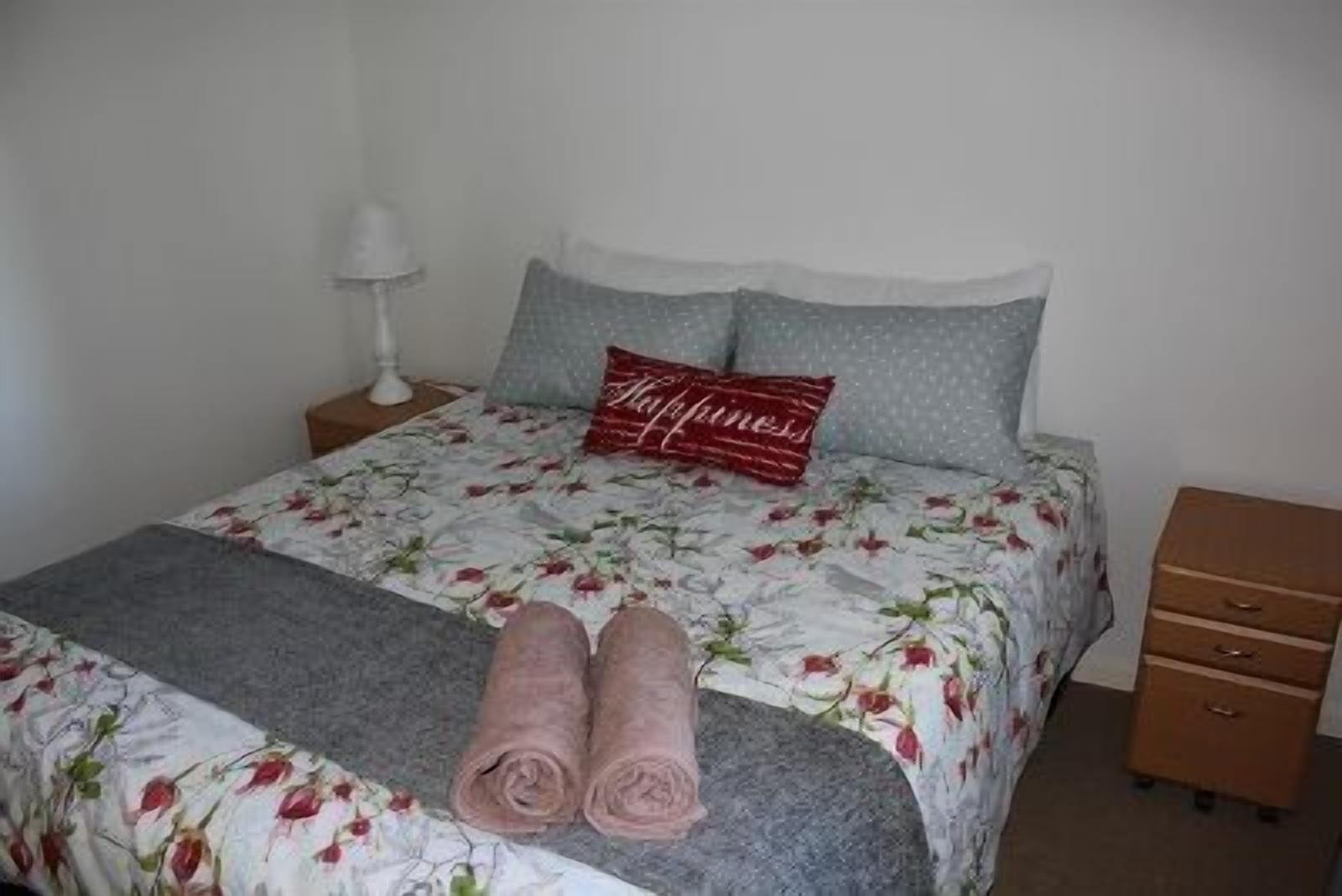 Un lit bien fait, avec une literie à motifs floraux, un coussin rouge et des serviettes enroulées posées sur le sol.
