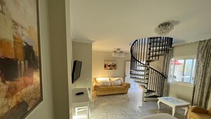 A hotel room with a bed, a sofa, a TV, a painting, a staircase, and a window. - Paraiso del Mar (Nerja)