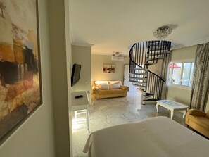 A hotel room with a bed, a sofa, a TV, a painting, a staircase, and a window. - Paraiso del Mar (Nerja)
