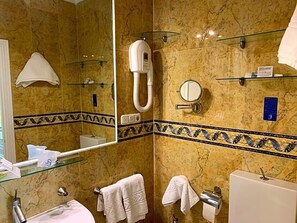 Ein Badezimmer mit Duschkabine aus Glas, einer Handbrause, einem Waschbecken mit Spiegel und Handtüchern auf Ablagen.