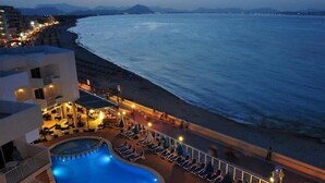 Un área de piscina con sillones de descanso, una piscina y vista a la playa y al océano.