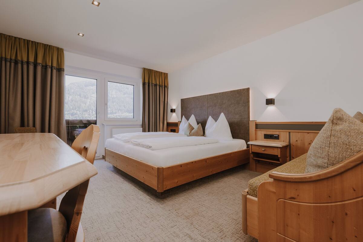 Ein Hotelzimmer mit einem hölzernen Bett, einem Schreibtisch aus Holz, einem Sessel, einem Nachttisch und einem großen Fenster.