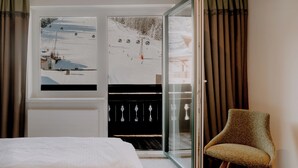 A hotel room with a bed, a chair, a window with a ski slope view, and a sliding glass door. - B&B Hotel Die Bergquelle (Flachau)