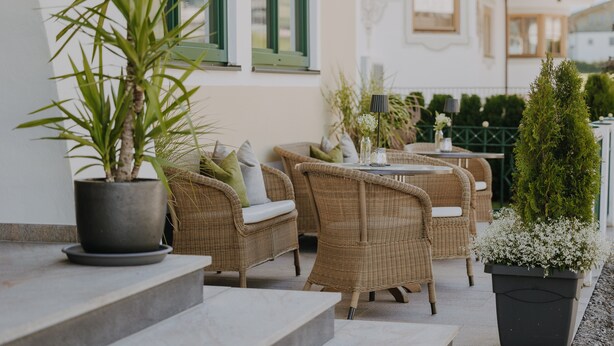 An outdoor seating area with wicker furniture, potted plants, and a staircase leading to an upper level. - B&B Hotel Die Bergquelle (Flachau)