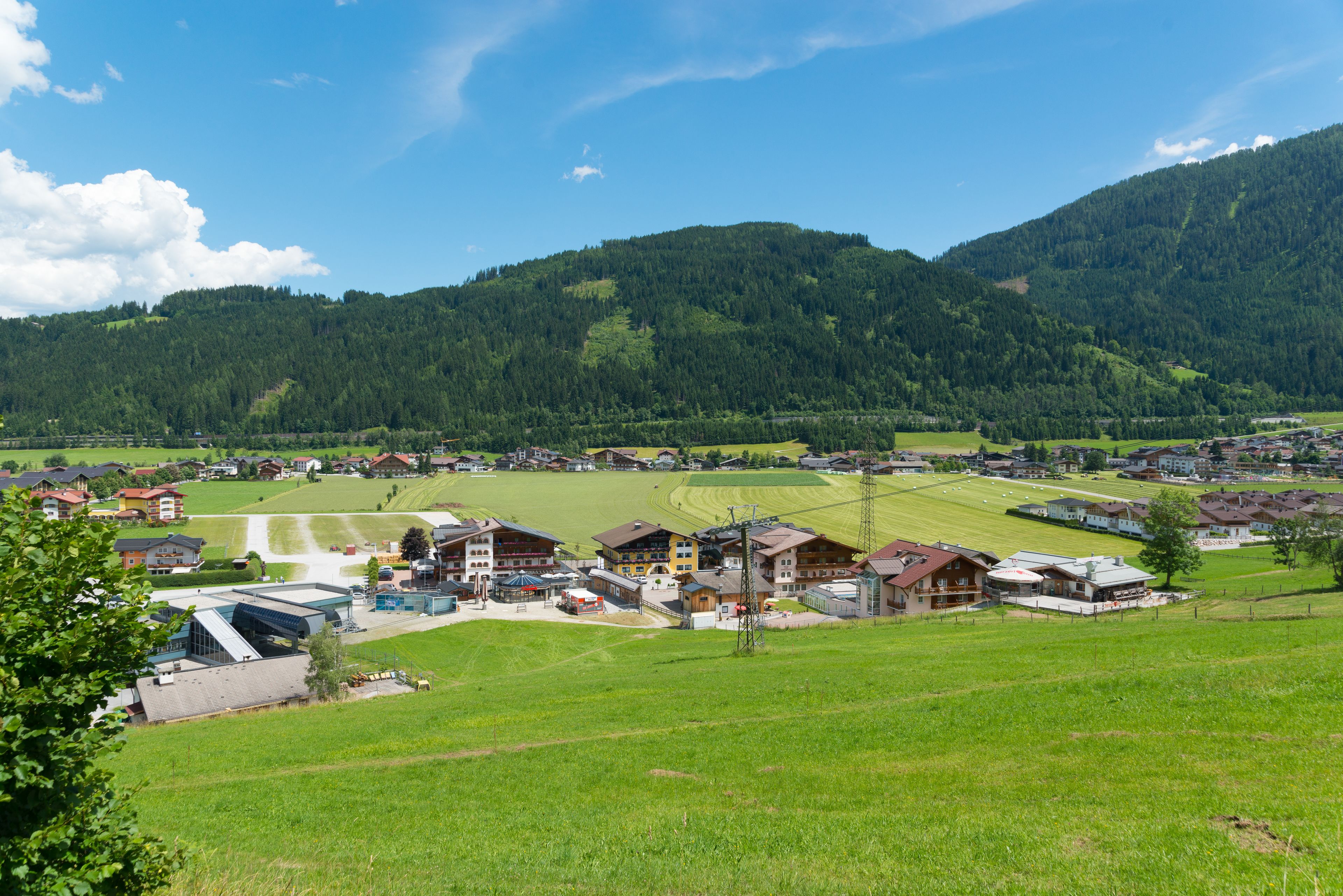 Ein ländliches Dorf mit Häusern, einem kleinen Gebäude mit Satteldach und einem grünen Feld.